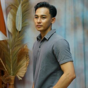 A portrait of a young man standing indoors with a creative backdrop, exuding calm and style.